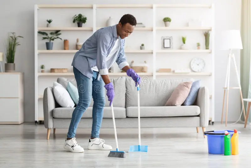 cheerful black guy cleaning living room holding broom handsome cozy alone scoop copy space smiling african american young man 220200003